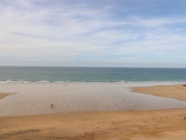 A sandy beach with a few people near the water and the ocean in the background at King Edward's View in Newquay