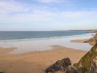 A wide sandy beach with few people walking near the sea and rocky cliffs at King Edward's View in Newquay