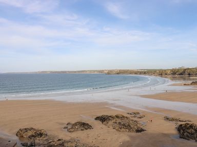 A sandy beach with rocks and people walking near the water at King Edward's View in Newquay