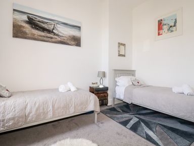 A bedroom with two single beds, bedside table with lamp, wall art, and a patterned rug at King Edward's View in Newquay