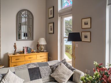 A living room with a patterned sofa cushions floor lamp wooden sideboard with books and sculptures and framed pictures on the walls at King Edward's View in Newquay