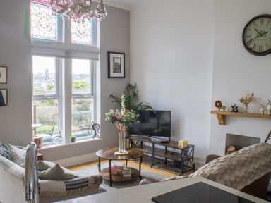 A living room with a television a round wooden coffee table with flowers and large windows at King Edward's View in Newquay