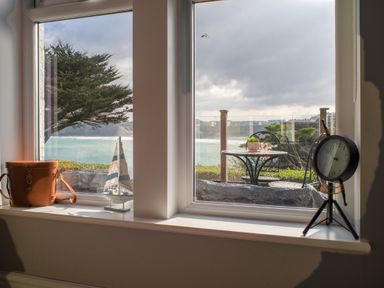 A window view showing a tree and ocean outside with a small decorative sailboat and a clock on the windowsill at King Edward's View in Newquay