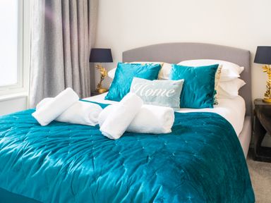 A bed with rolled towels and pillows on a turquoise bedspread in a bedroom at King Edward's View in Newquay