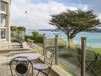 A patio with mosaic table and chairs overlooking a tree hedge and sea at King Edward's View in Newquay
