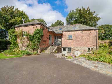 A brick house with a sloped roof and stairs leading to the front door surrounded by trees and plants at The Old Watermill in St Mabyn