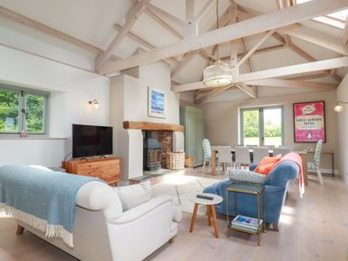 A living room with sofas a fireplace a dining table and large wooden beams at The Old Watermill in St Mabyn