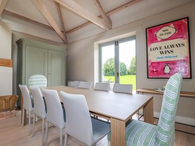 A dining room with a wooden table white chairs striped upholstered chairs and a large framed artwork near French doors at The Old Watermill in St Mabyn
