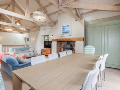 A dining table with white chairs next to a fireplace and sofas in a living room at The Old Watermill in St Mabyn