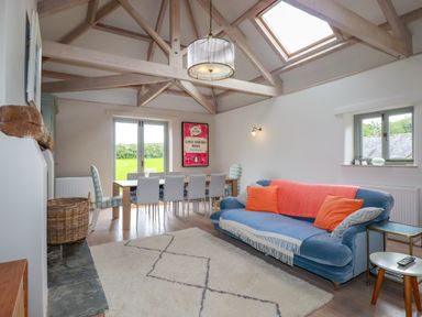 A living room with blue sofa orange pillows dining table and chairs under a wooden beam ceiling at The Old Watermill in St Mabyn