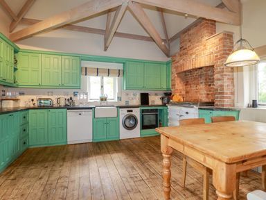 A kitchen with green cabinets a wooden dining table a brick fireplace and wooden ceiling beams at The Old Watermill in St Mabyn