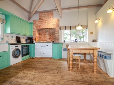 A kitchen with green cabinets a wooden dining table and a brick fireplace at The Old Watermill in St Mabyn
