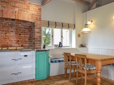 A kitchen with a brick oven area a white stove a turquoise cabinet a wooden dining table with two chairs and a built-in bench under a window at The Old Watermill in St Mabyn
