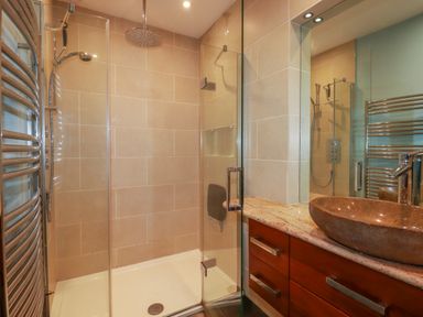 A bathroom with glass shower enclosure stone basin on wooden vanity and heated towel rail at The Old Watermill in St Mabyn