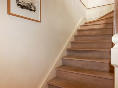 A wooden staircase with a white wall and framed artwork at The Old Watermill in St Mabyn