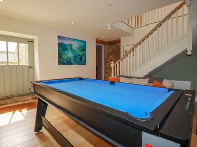 A room with a blue pool table, a staircase with a white railing, a sofa with cushions, and a painting on the wall at The Old Watermill in St Mabyn