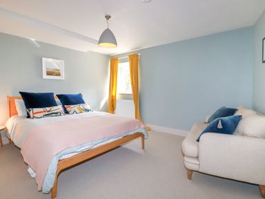 A bedroom with a bed and sofa with blue pillows and yellow curtains at The Old Watermill in St Mabyn