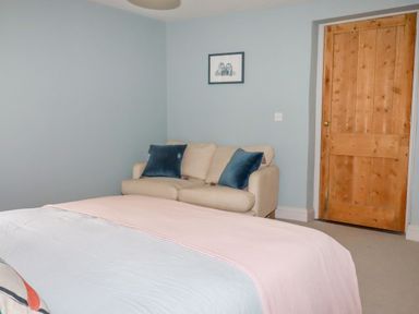 A bedroom with a beige sofa with blue cushions a wooden door and a bed with a pink blanket at The Old Watermill in St Mabyn