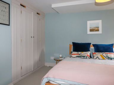 A bedroom with a bed with pillows and a pink blanket a side table with a lamp built-in wardrobes and framed artwork at The Old Watermill in St Mabyn
