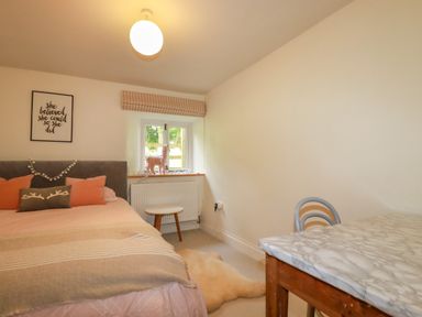 A bedroom with a bed, pillows, a stool under a window, a wall art, a chair and a table at The Old Watermill in St Mabyn