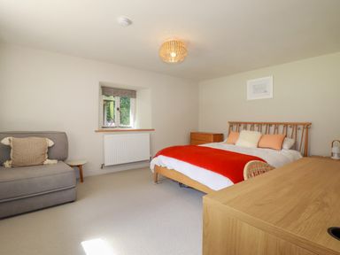 A bedroom with a bed with orange blanket pillows a gray chair a wooden desk and a small window at The Old Watermill in St Mabyn