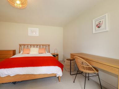 A bedroom with a bed a red blanket a wooden desk and chair and framed pictures on the wall at The Old Watermill in St Mabyn