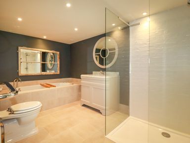 A bathroom with a bathtub a toilet a sink with round mirror and a glass enclosed shower at The Old Watermill in St Mabyn