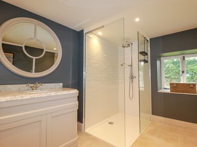 A bathroom with a shower enclosure a sink with a countertop and a round mirror at The Old Watermill in St Mabyn