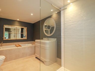 A bathroom with a bathtub a toilet a vanity with a round mirror and a glass shower enclosure at The Old Watermill in St Mabyn