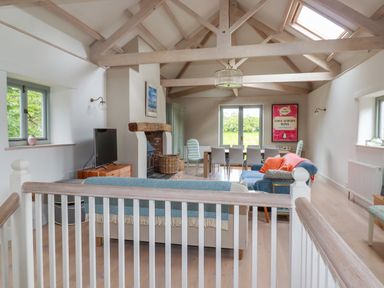 An open living and dining room with exposed ceiling beams a fireplace a television sofas and a dining table at The Old Watermill in St Mabyn