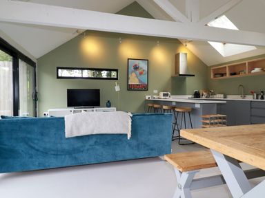 An open-plan living room and kitchen with a blue sofa a wooden dining table and bar stools at The Old Watermill in St Mabyn