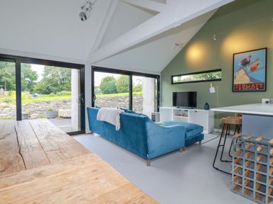 A living room with a blue sofa tv and large windows at The Old Watermill in St Mabyn