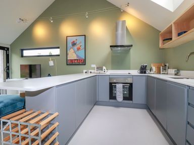 A kitchen with grey cabinets white countertops a built in oven and stove a toaster and coffee maker on the counter at The Old Watermill in St Mabyn