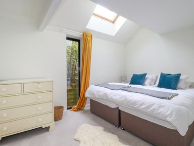 A bedroom with a double bed with blue pillows a cream chest of drawers a skylight window and mustard curtain at The Old Watermill in St Mabyn