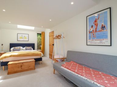 A bedroom with a bed yellow blanket gray sofa wooden chest and clothing rack at The Old Watermill in St Mabyn