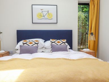 A bedroom with a bed with patterned and plain pillows and yellow blanket beside a window with yellow curtains at The Old Watermill in St Mabyn