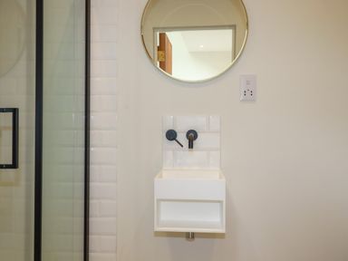 A small wall mounted sink with black taps and a round mirror above at The Old Watermill in St Mabyn