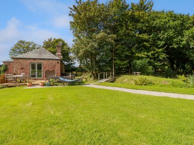 A backyard with a brick house patio table hammock grassy lawn small wooden bridge and trees at The Old Watermill in St Mabyn
