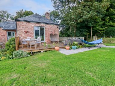 A brick house with a wooden deck patio set and hammock in a garden at The Old Watermill in St Mabyn