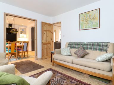A living room with a beige sofa with cushions and a plaid blanket a framed map on the wall and doorways leading to a dining area and kitchen at Yamthwaite in Grizedale near Hawkshead