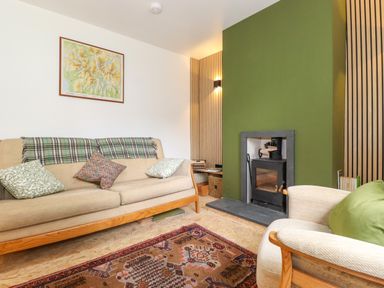 A living room with a beige sofa and armchair a patterned rug and a green fireplace at Yamthwaite in Grizedale near Hawkshead