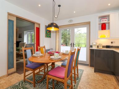 A dining area with a wooden table and colorful chairs next to kitchen cabinets and glass doors at Yamthwaite in Grizedale near Hawkshead