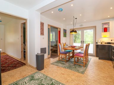 A kitchen dining area with a wooden round table and colorful chairs near glass doors at Yamthwaite in Grizedale near Hawkshead