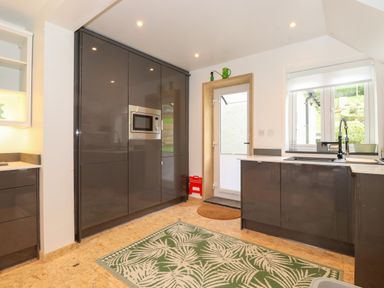 A kitchen with dark cabinets a built in microwave a sink under a window and a green patterned rug on the floor at Yamthwaite in Grizedale near Hawkshead