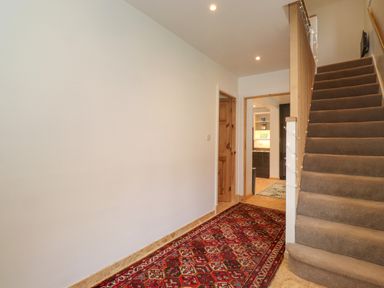 A hallway with a patterned red carpet leading to an open door and a staircase with carpet at Yamthwaite in Grizedale near Hawkshead