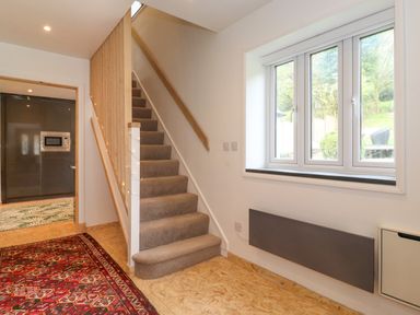 A hallway with carpeted stairs next to a window and a kitchen visible through the doorway at Yamthwaite Grizedale near Hawkshead