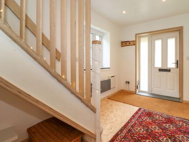 An entrance hallway with a white front door wooden staircase and a red patterned rug at Yamthwaite in Grizedale near Hawkshead
