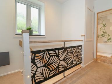 A hallway with a window and decorative railing next to a bathroom with a bathtub at Yamthwaite in Grizedale near Hawkshead