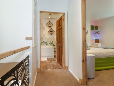 A hallway with wooden door leading to a bathroom with a bathtub and plants and a bedroom with a bed and towels at Yamthwaite in Grizedale near Hawkshead