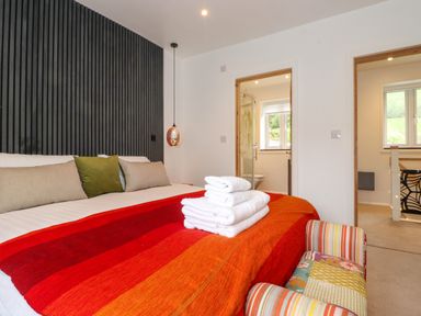 A bedroom with a bed covered by a red and orange blanket and folded towels on top at Yamthwaite Grizedale near Hawkshead